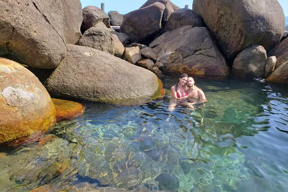 Casal curtindo as piscinas naturais com rochas ao fundo, em Ihabela